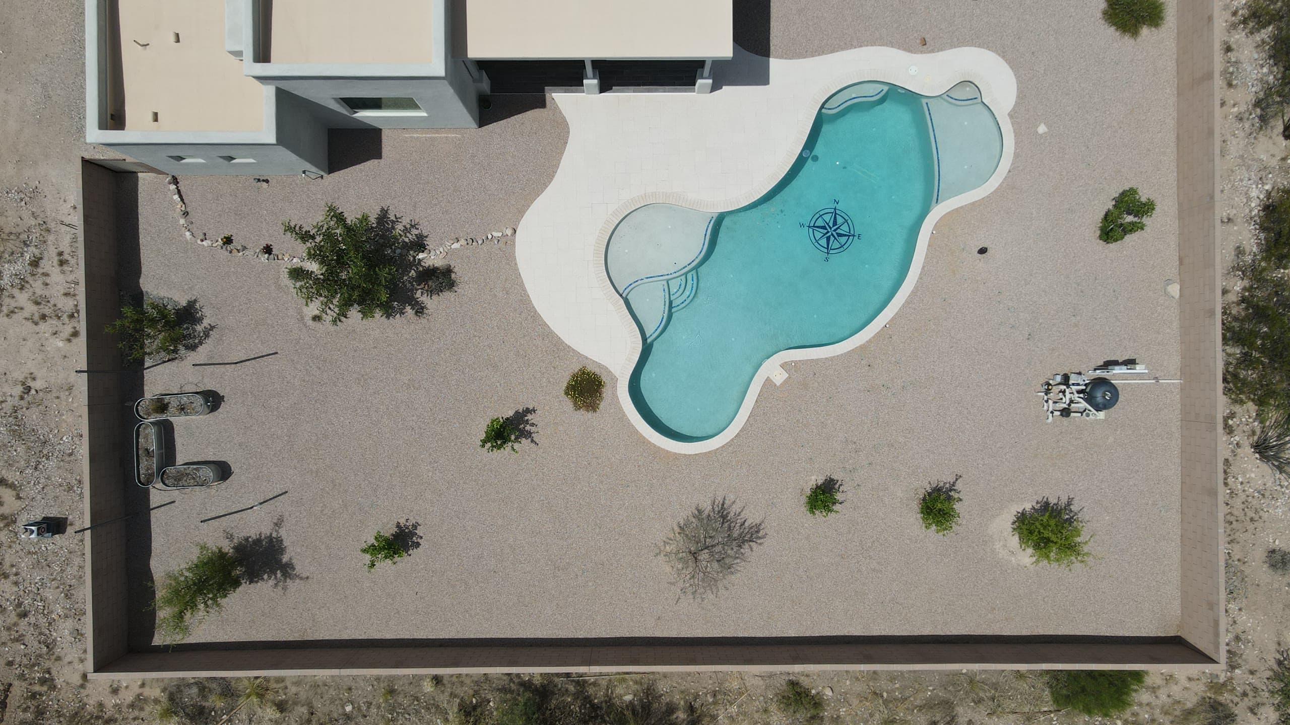 Overhead view of a freeform pool with a compass-rose tile in a gravel yard