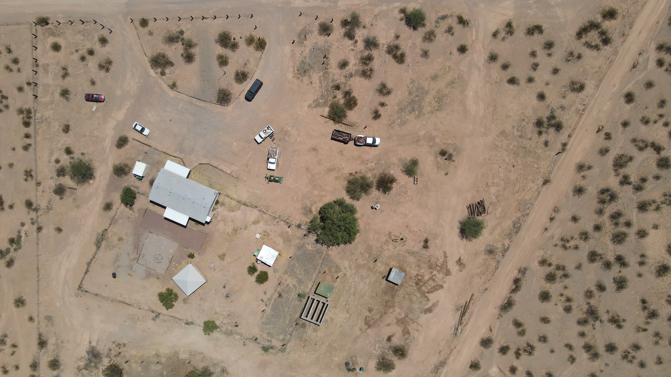 Overhead view of a fenced desert parcel with a home site and outbuildings