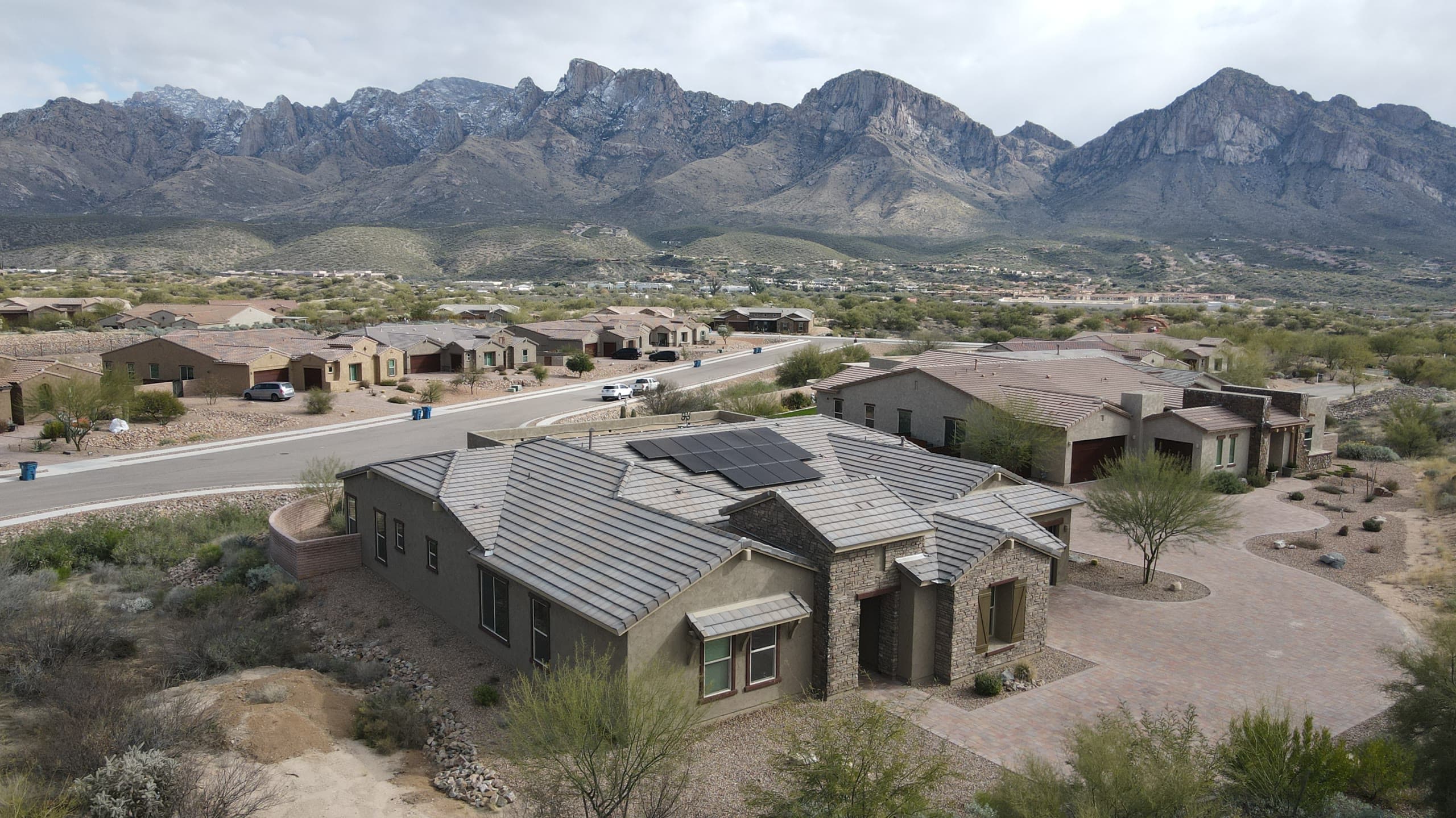 Single-story stone and stucco home with rooftop solar, snow-dusted Santa Catalina Mountains behind
