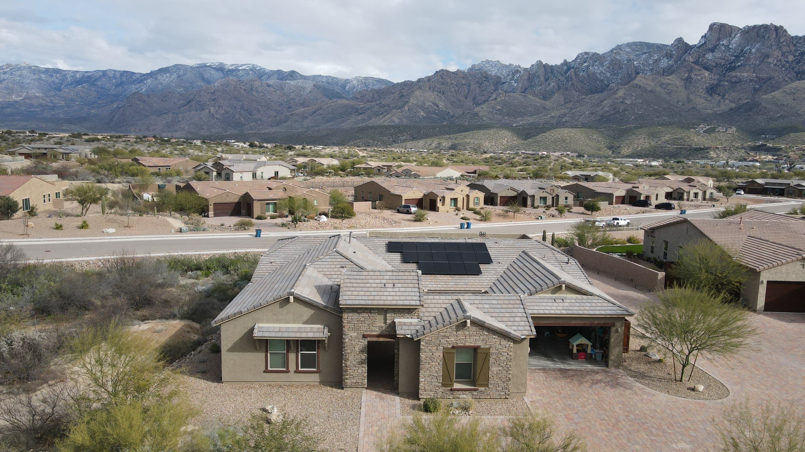 Front of a stone and stucco home with a paver drive and the Catalinas behind